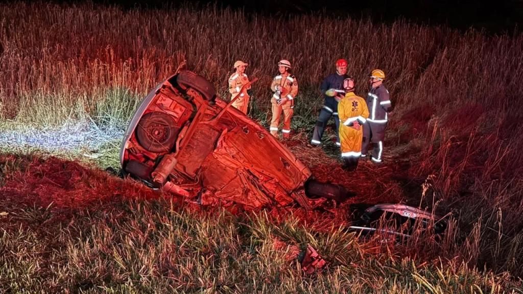 Veículo Ford Ka completamente destruído após colisão frontal com carreta na BR-277, com destroços espalhados e carreta fora da pista em meio à vegetação.